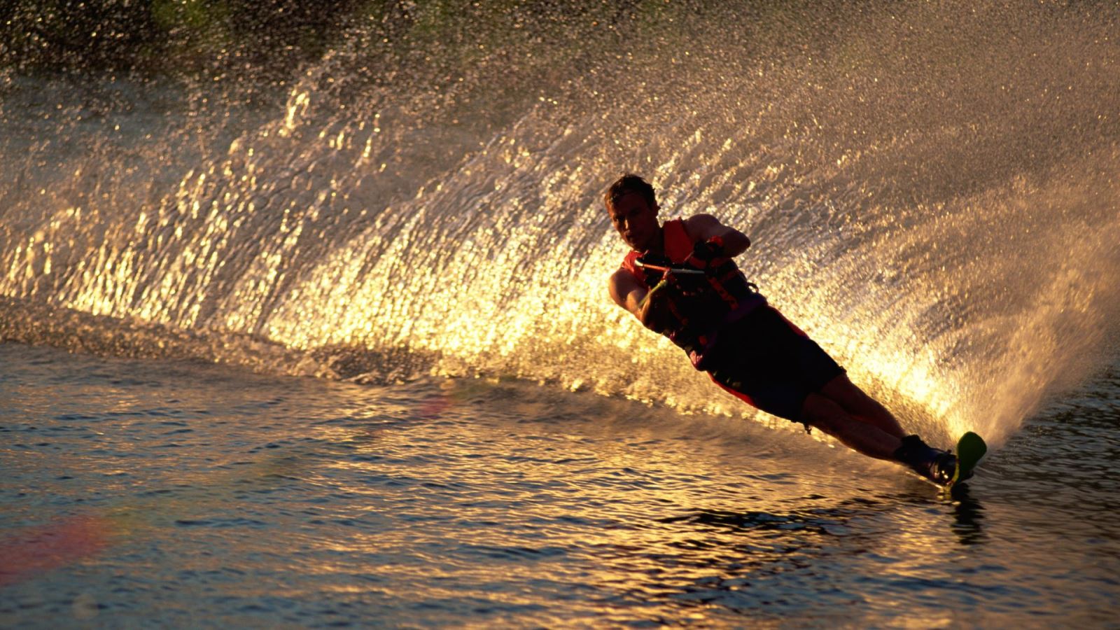 A water skier silhouetted against a golden sunset and spray